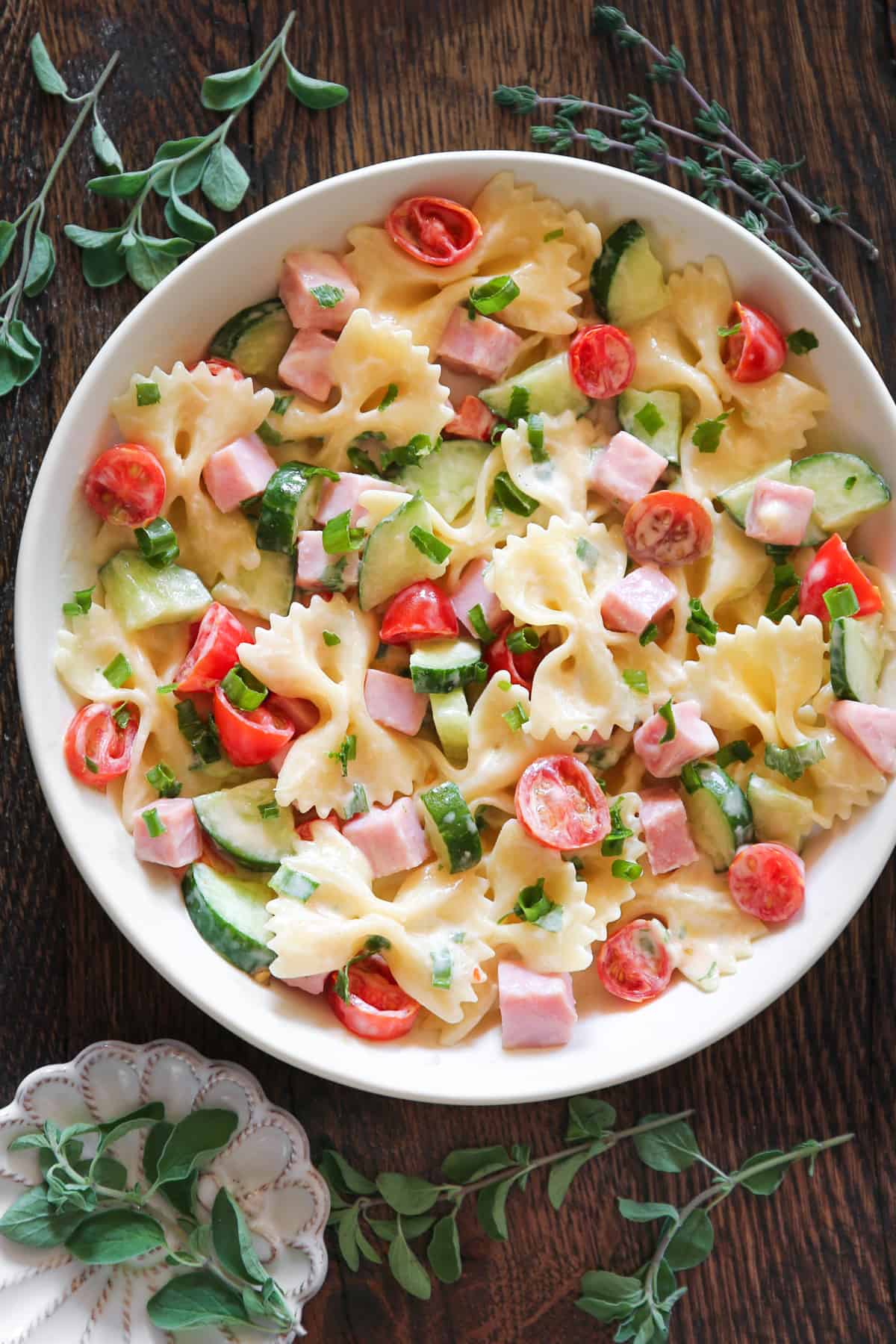Creamy Ham Pasta Salad with Cherry Tomatoes, Cucumbers, and Green Onions in a white bowl.