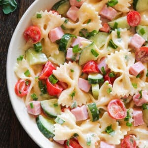 Creamy Ham Pasta Salad with Cherry Tomatoes, Cucumbers, and Green Onions in a white bowl.