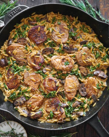Creamy Pork Tenderloin Medallions with Orzo, Spinach, and Mushrooms - in a cast iron skillet.