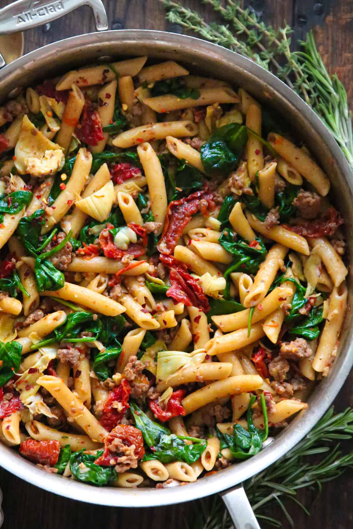 Italian Sausage Pasta with Spinach, Artichokes, and Sun-Dried Tomatoes - in a stainless steel skillet.