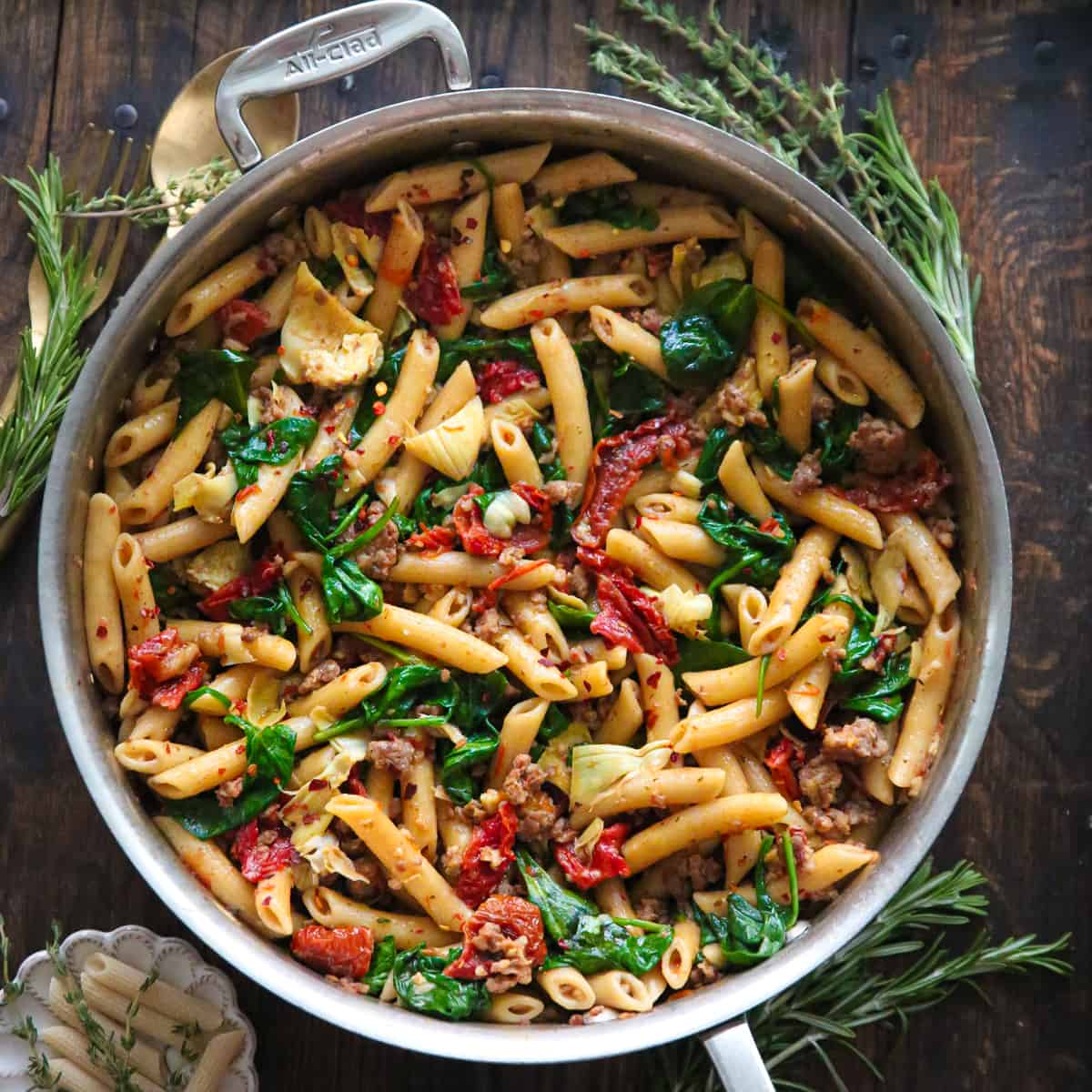 Italian Sausage Pasta with Spinach, Artichokes, and Sun-Dried Tomatoes - in a stainless steel skillet.