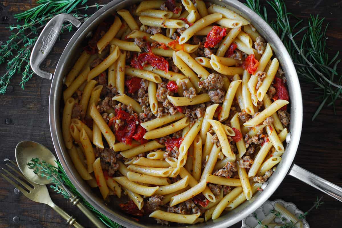 Italian sausage rigatoni pasta with sun-dried tomatoes in a stainless steel skillet.