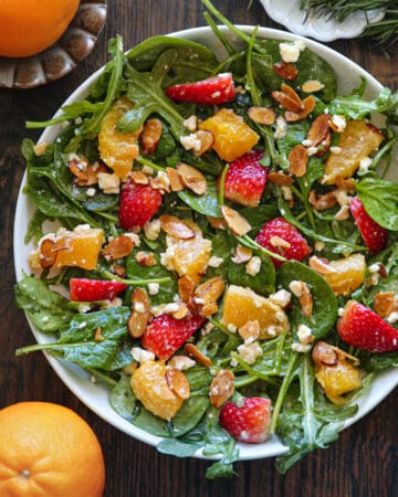 Strawberry Orange Salad with Spinach, Arugula, Toasted Sliced Almonds, and Feta Cheese - in a white bowl.