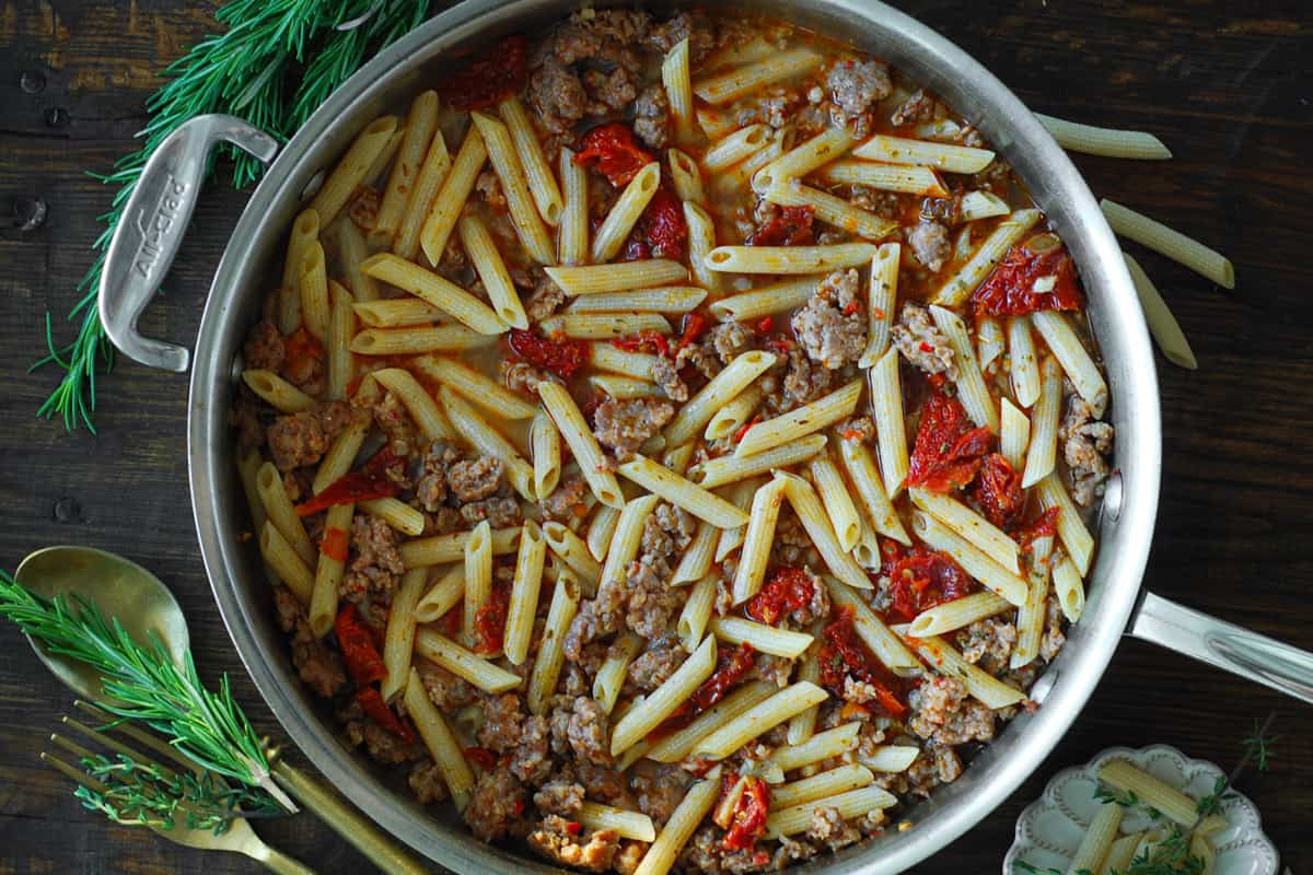 cooked sausage, rigatoni, and sun-dried tomatoes in a stainless steel skillet.