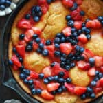 Dutch baby pancake with honey-lemon cooked strawberries and blueberries - in a cast iron skillet.