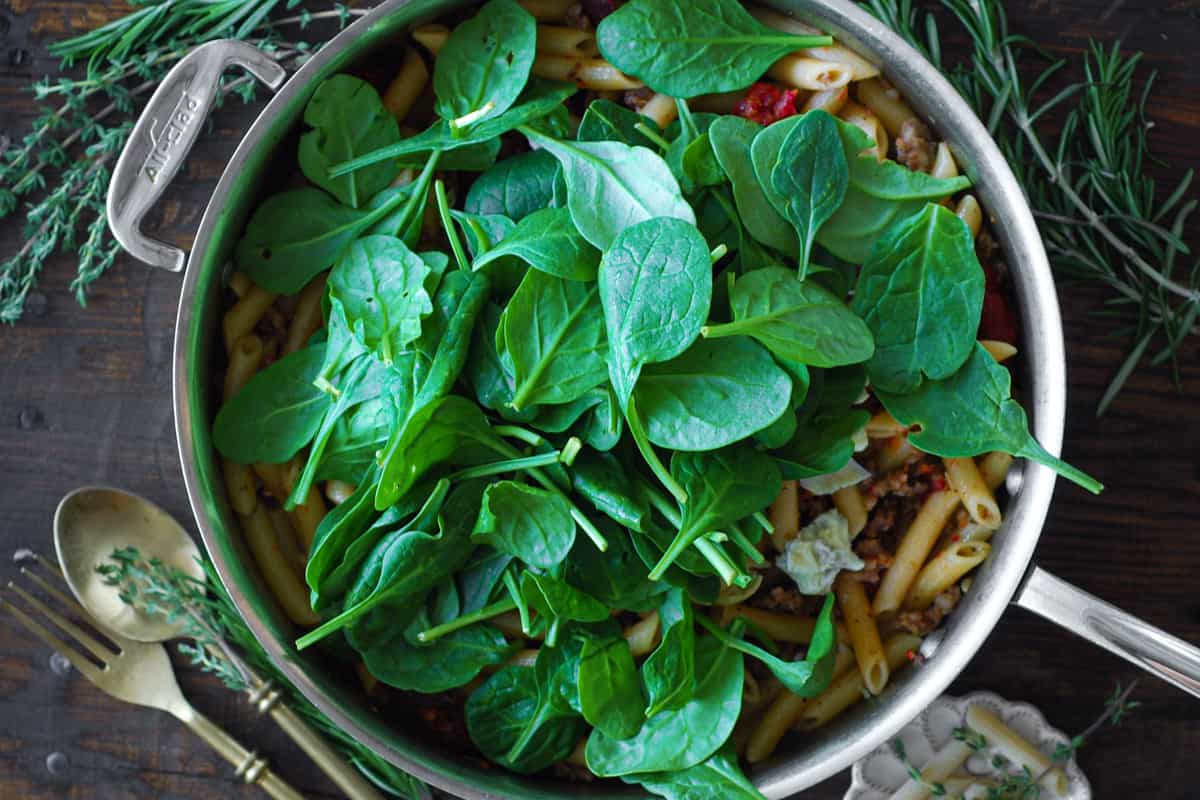fresh spinach and pasta in a stainless steel skillet.