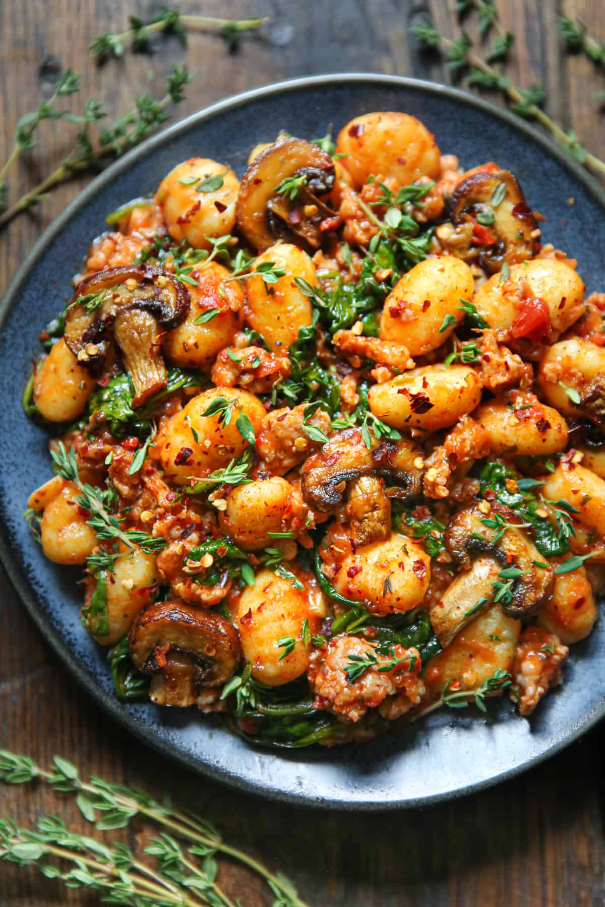 gnocchi with tomato sauce, sausage, spinach, and mushrooms on a blue plate.