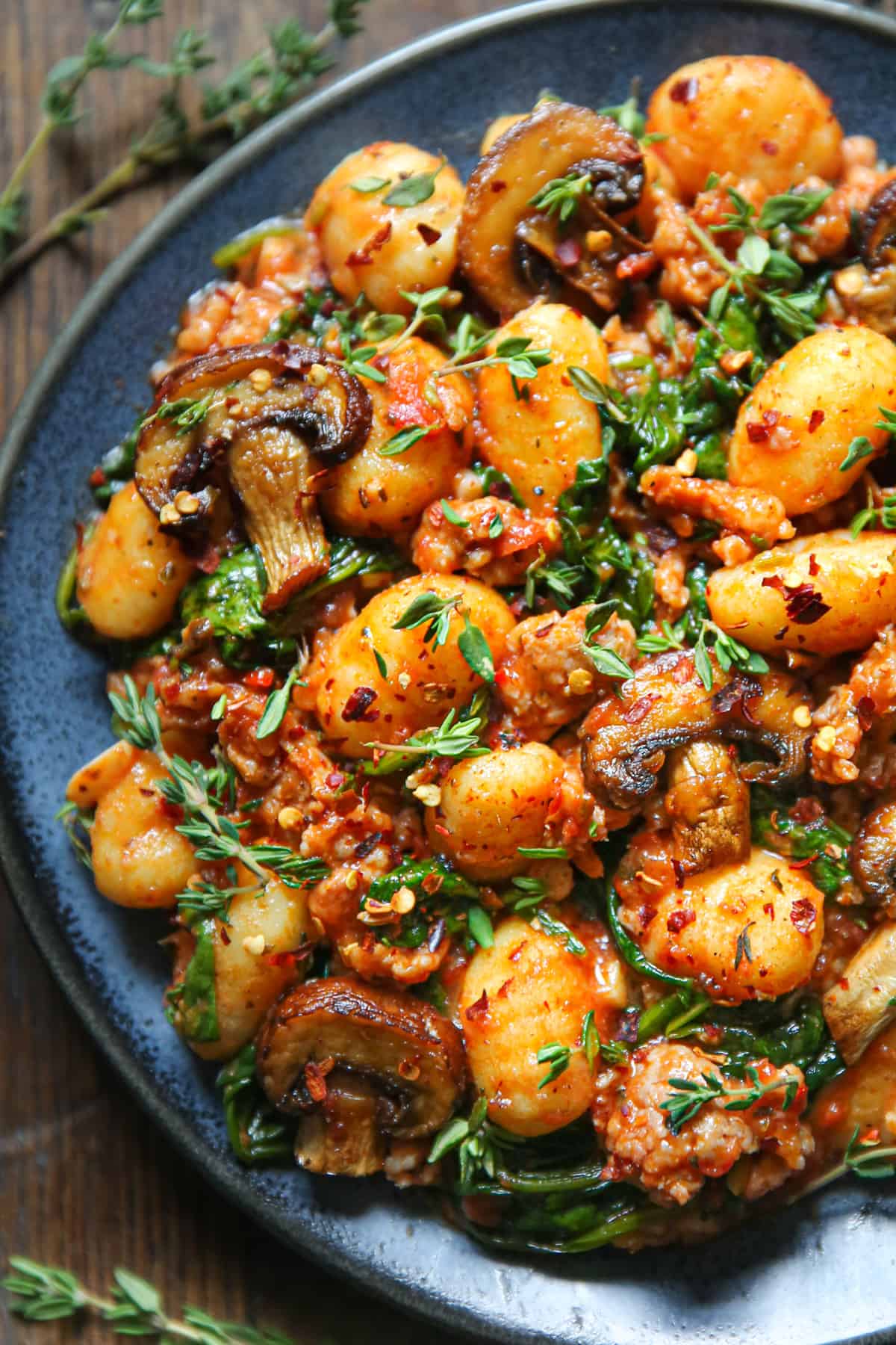 gnocchi with tomato sauce, sausage, spinach, and mushrooms on a blue plate.