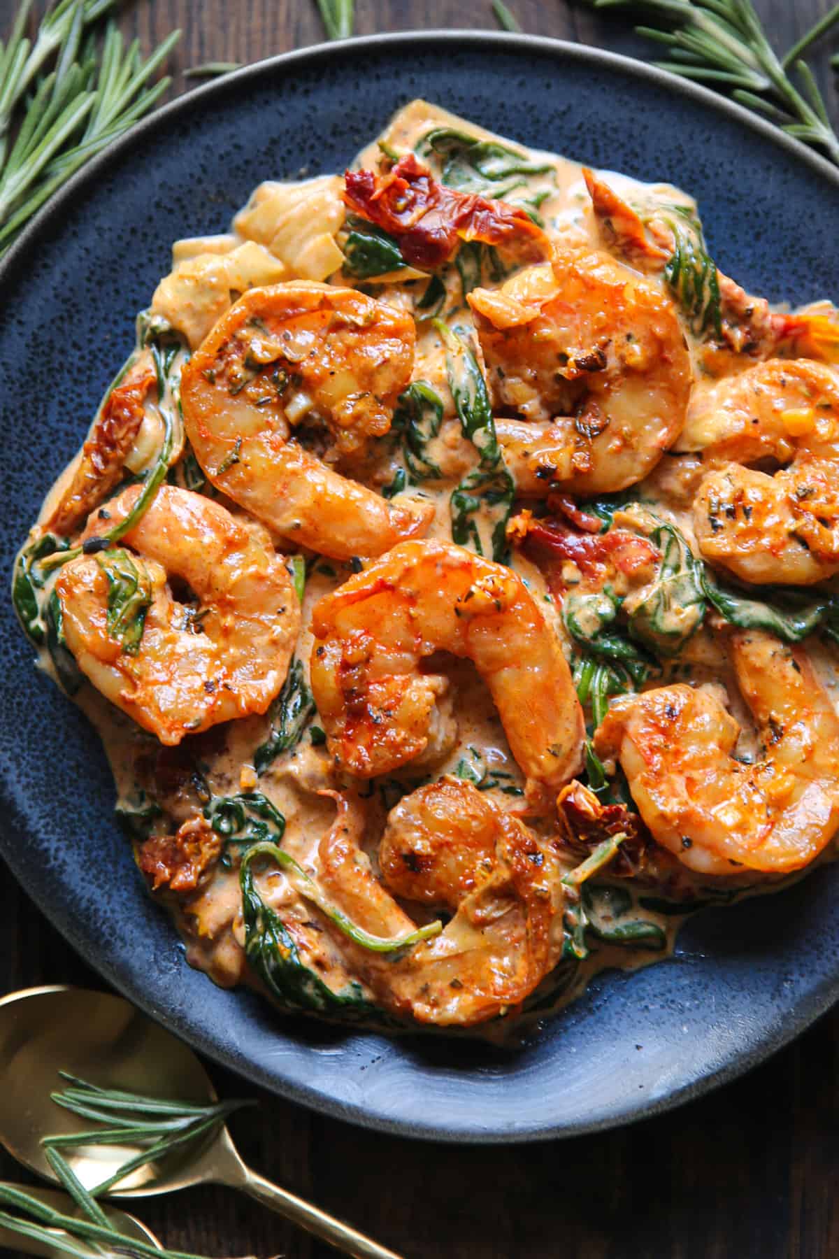 Creamy Tuscan Shrimp with Sun-Dried Tomatoes, Spinach, and Artichokes - on a blue plate.