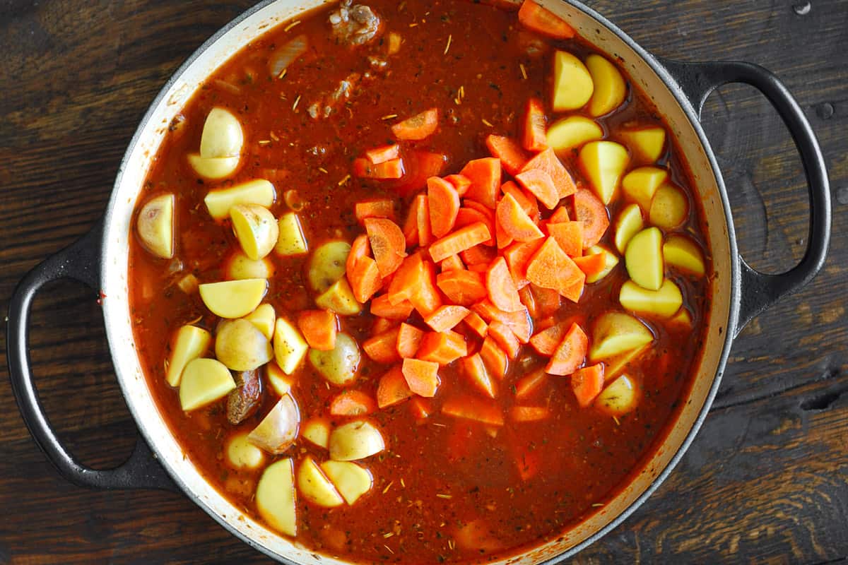 browned beef with onions, garlic, tomato paste, beef broth, sliced carrots, and quartered small potatoes - in a pot.