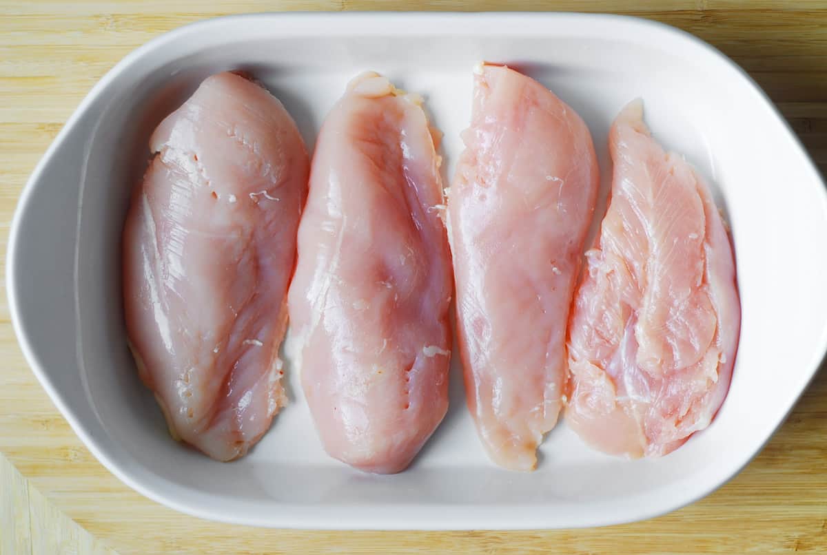 four chicken breasts in a casserole dish.