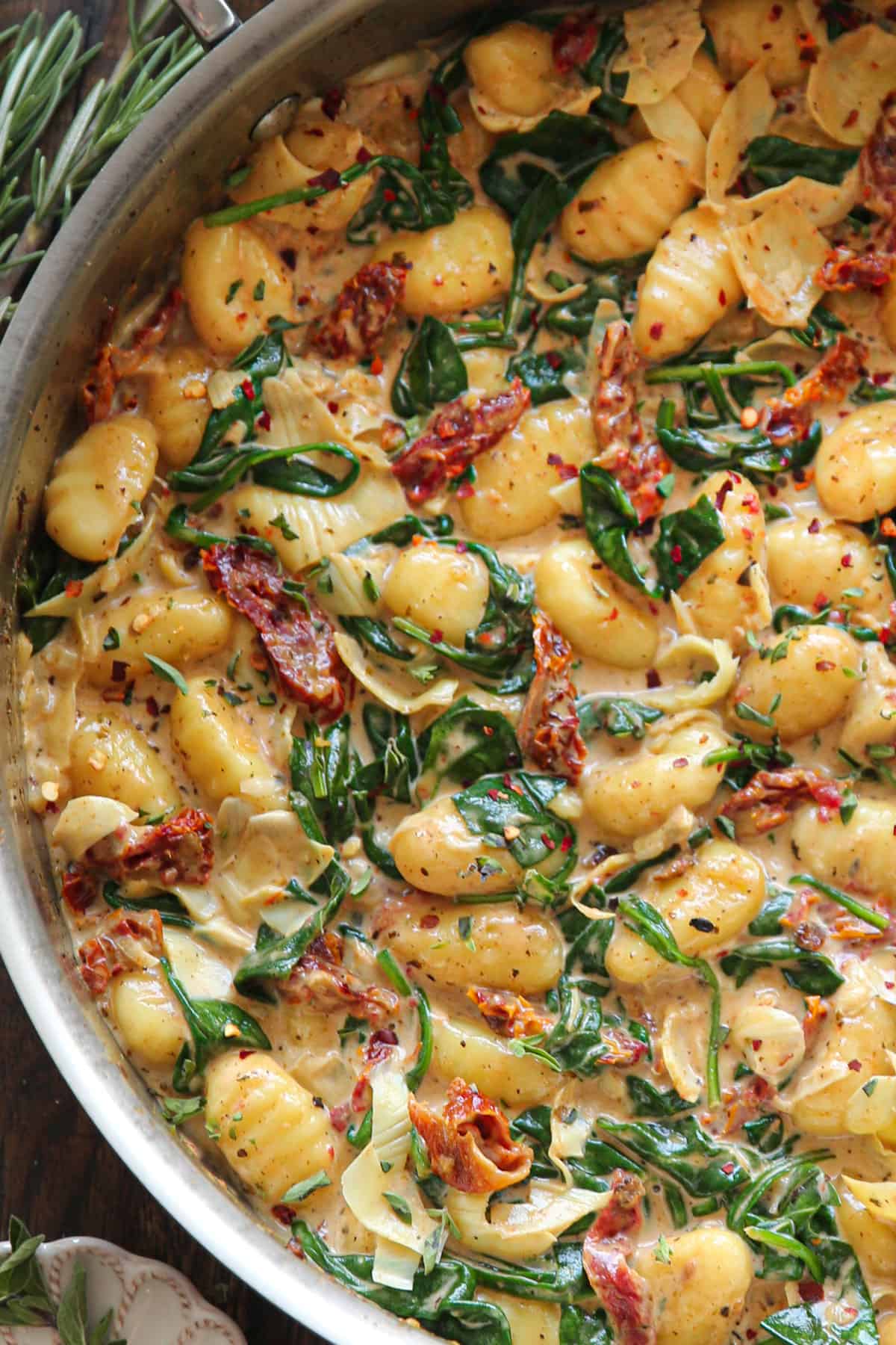 Creamy Tuscan Gnocchi with sun-dried tomatoes, spinach, and artichokes - in a stainless steel pan.
