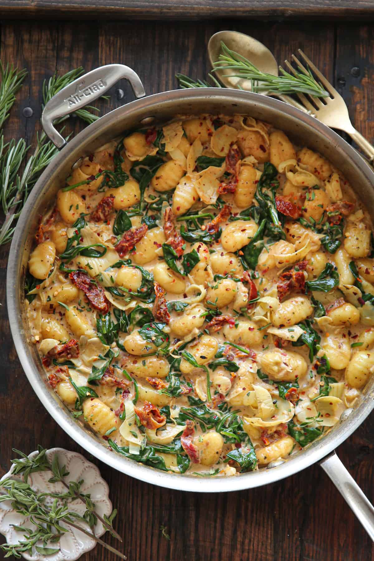 Creamy Tuscan Gnocchi with sun-dried tomatoes, spinach, and artichokes - in a stainless steel pan.