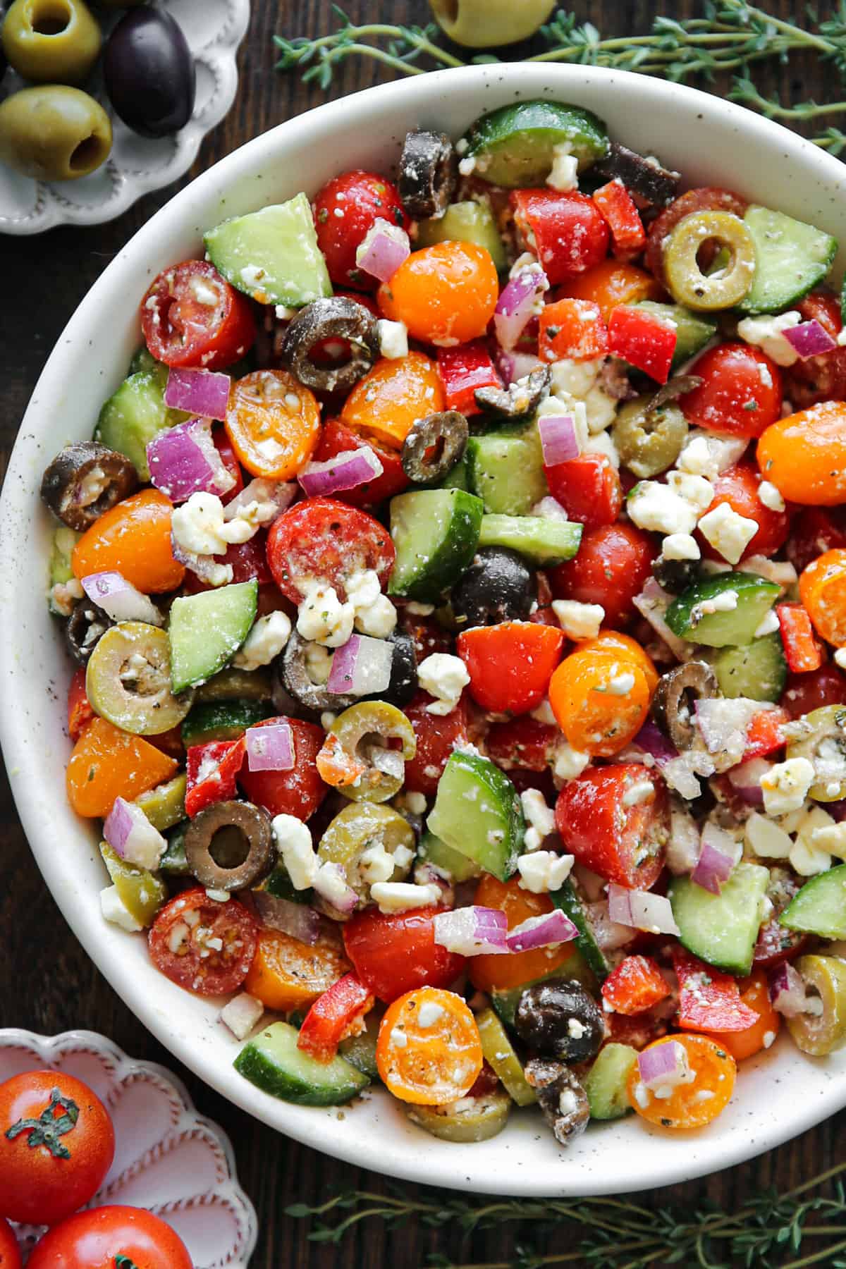 Greek salad with grape tomatoes, cucumber, bell pepper, olives, red onions, and feta cheese - in a white bowl.