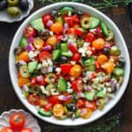 Greek salad with grape tomatoes, cucumber, bell pepper, olives, red onions, and feta cheese - in a white bowl.