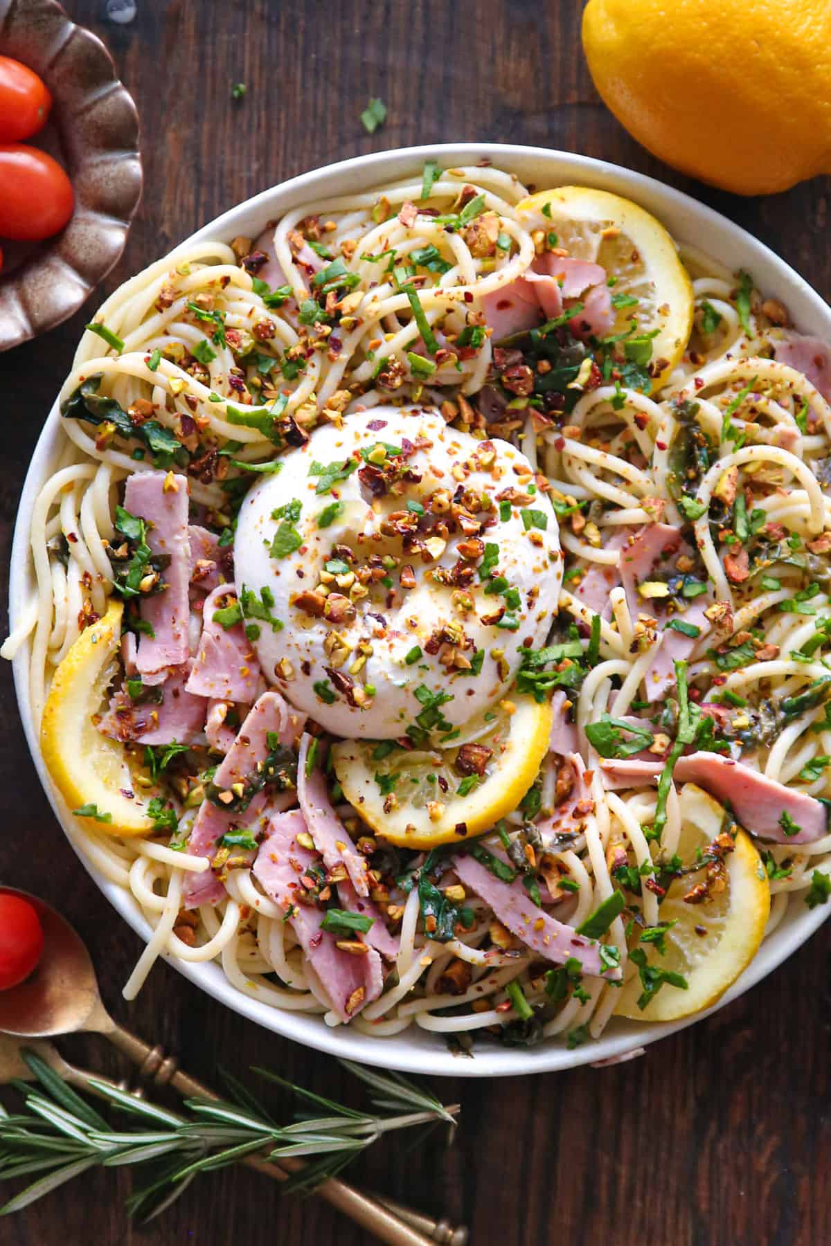 Ham spaghetti pasta with Burrata cheese, spinach, and chopped pistachios - in a white bowl.