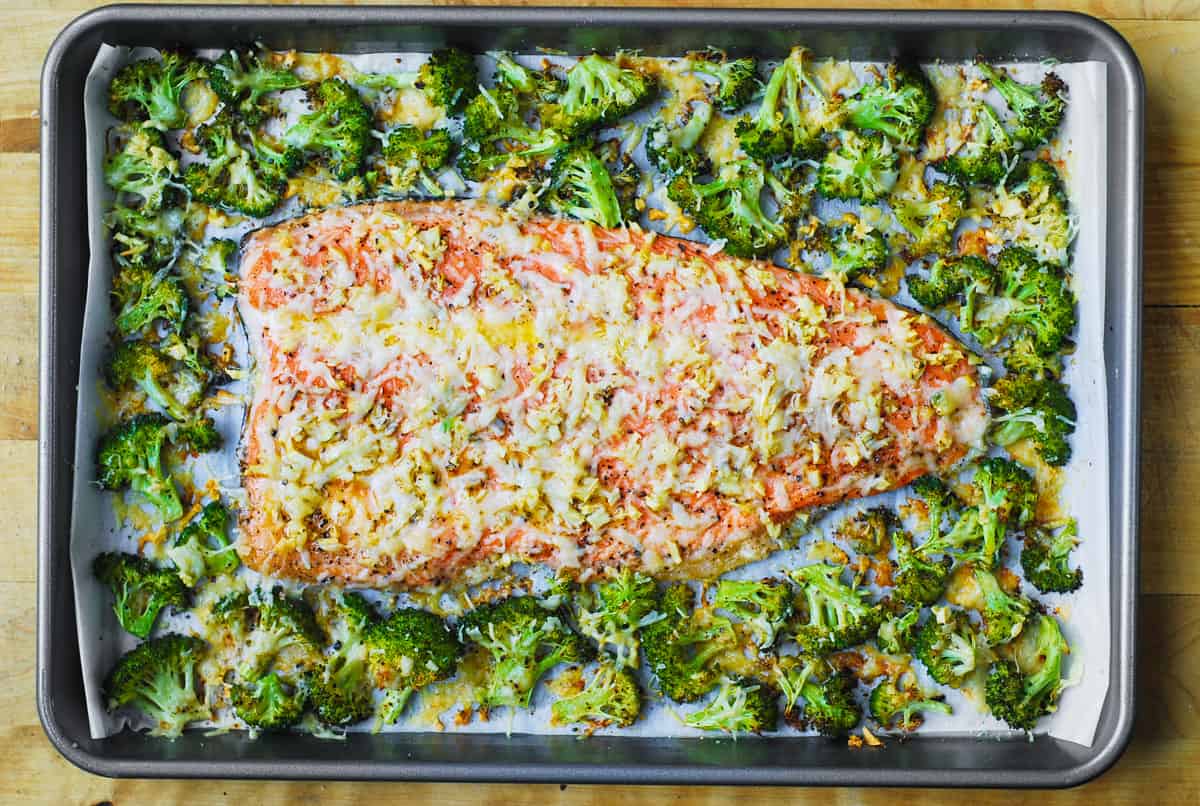 baked salmon and broccoli with minced garlic and shredded Parmesan Cheese on a sheet pan.