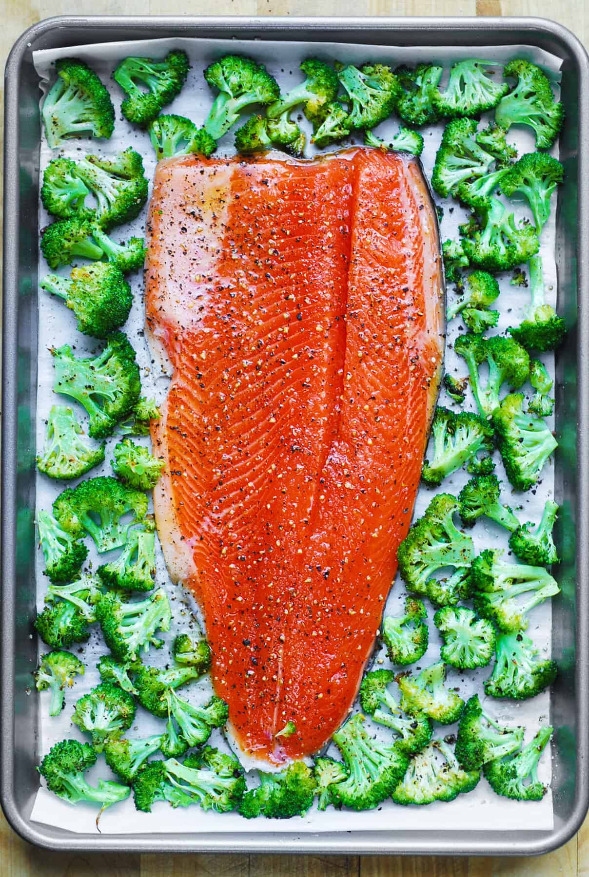 Sheet Pan Salmon and Broccoli seasoned with salt and pepper.
