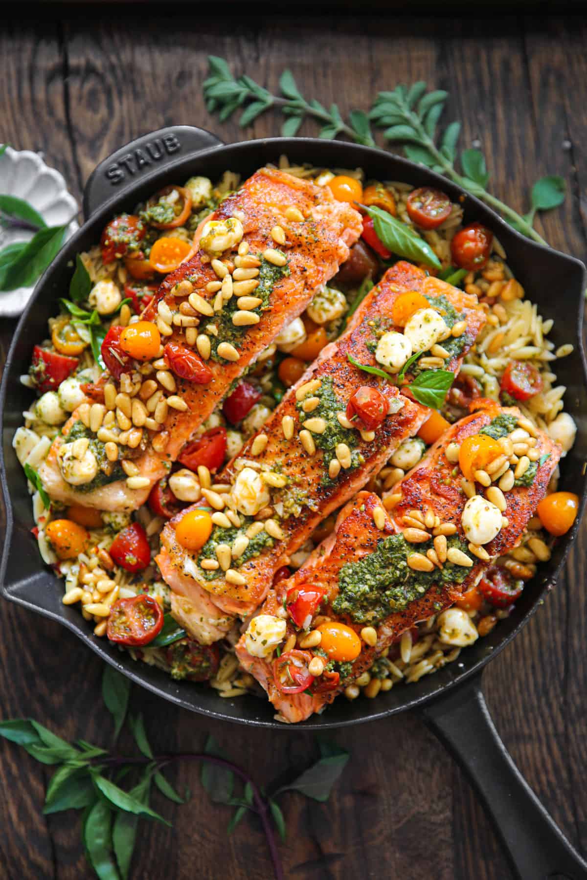 Salmon fillets with orzo, basil pesto, grape tomatoes, Mozzarella cheese, and pine nuts - in a cast iron skillet.