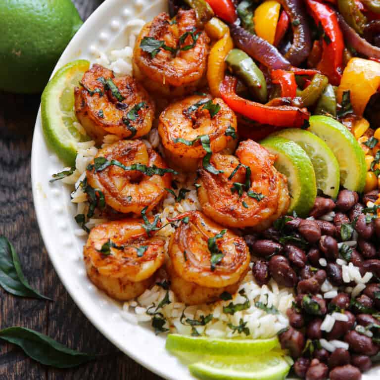 Shrimp Fajita bowl with bell peppers, red onions, black beans, corn, rice, and lime slices.
