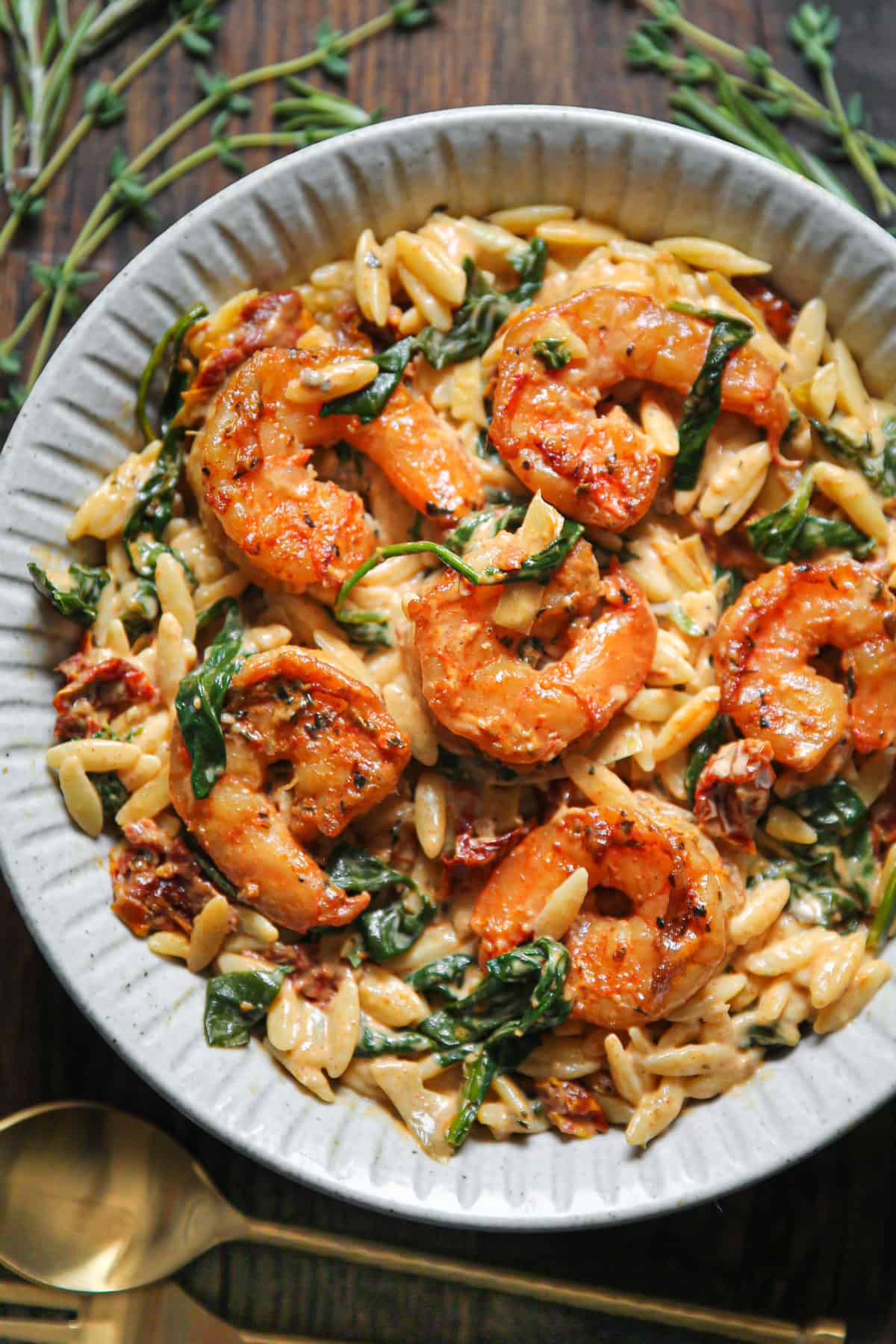 Creamy shrimp rice with spinach, sun-dried tomatoes and artichokes - in a white bowl.