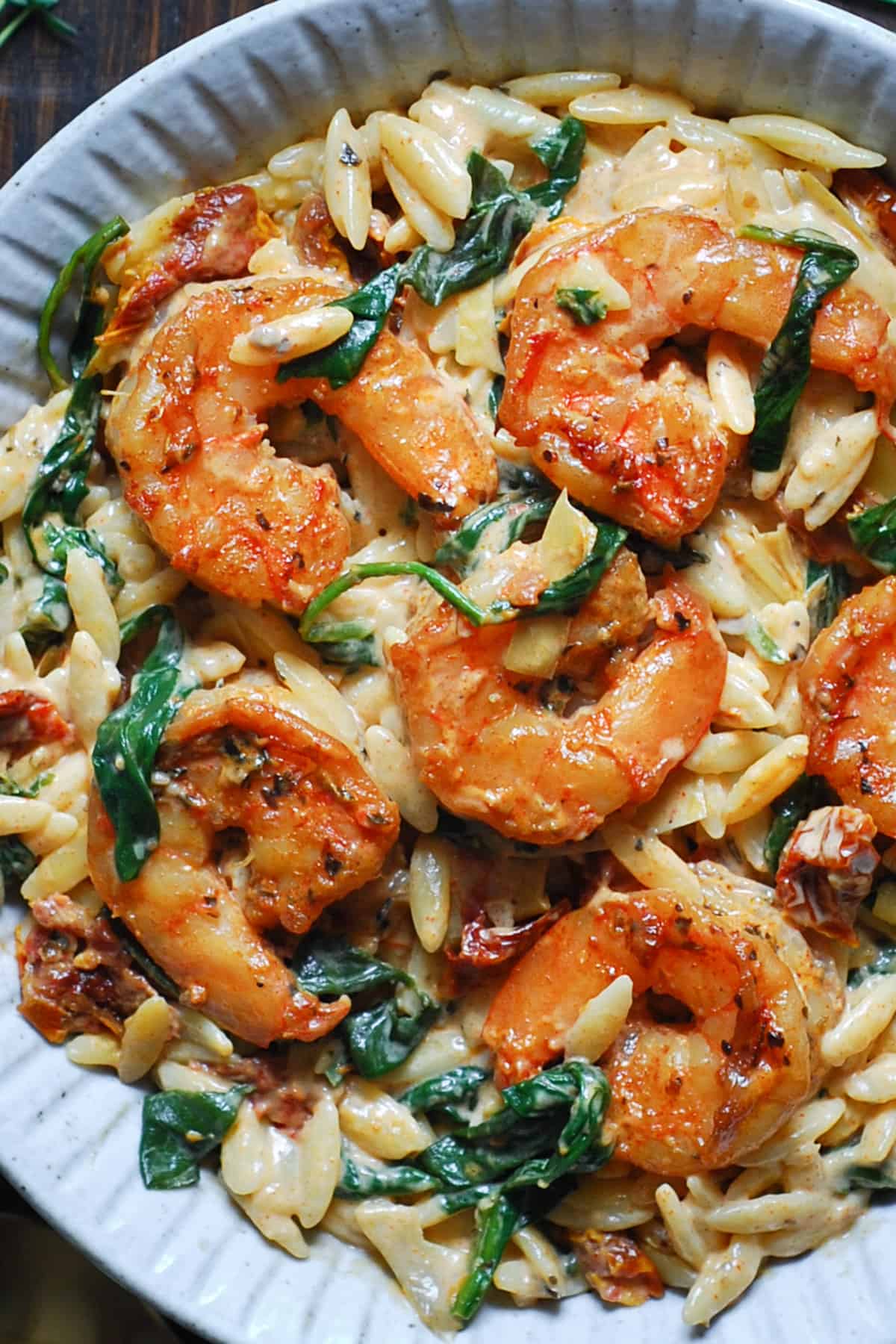 Creamy Shrimp Orzo with Spinach, Sun-Dried Tomatoes, and Artichokes - in a white bowl.
