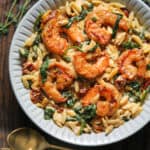 Creamy Shrimp Orzo with Sun-Dried Tomatoes, Spinach, Artichokes - in a white bowl.
