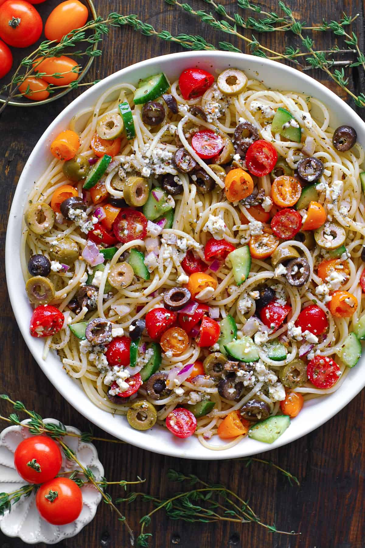 Spaghetti Salad with cherry (or grape) tomatoes, cucumbers, black olives, green olives, red onion, and feta cheese - in a white bowl.