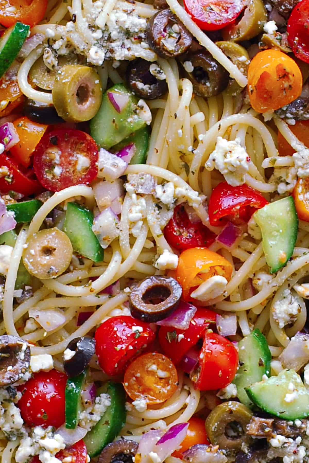 Spaghetti Salad with cherry (or grape) tomatoes, cucumbers, black olives, green olives, red onion, and feta cheese - close-up photo.