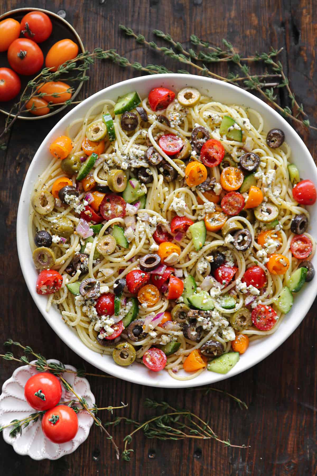 Spaghetti Salad with cherry (or grape) tomatoes, cucumbers, black olives, green olives, red onion, and feta cheese - in a white bowl.