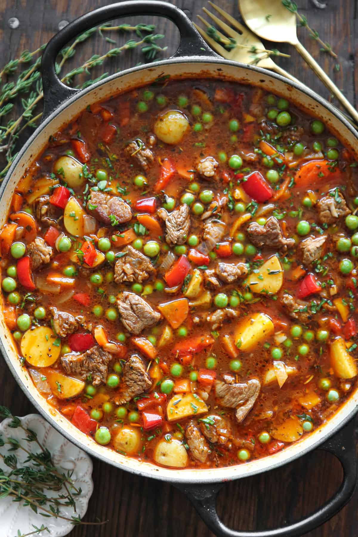 Vegetable beef soup with onions, garlic, carrots, potatoes, bell peppers, and green peas - in a pot.