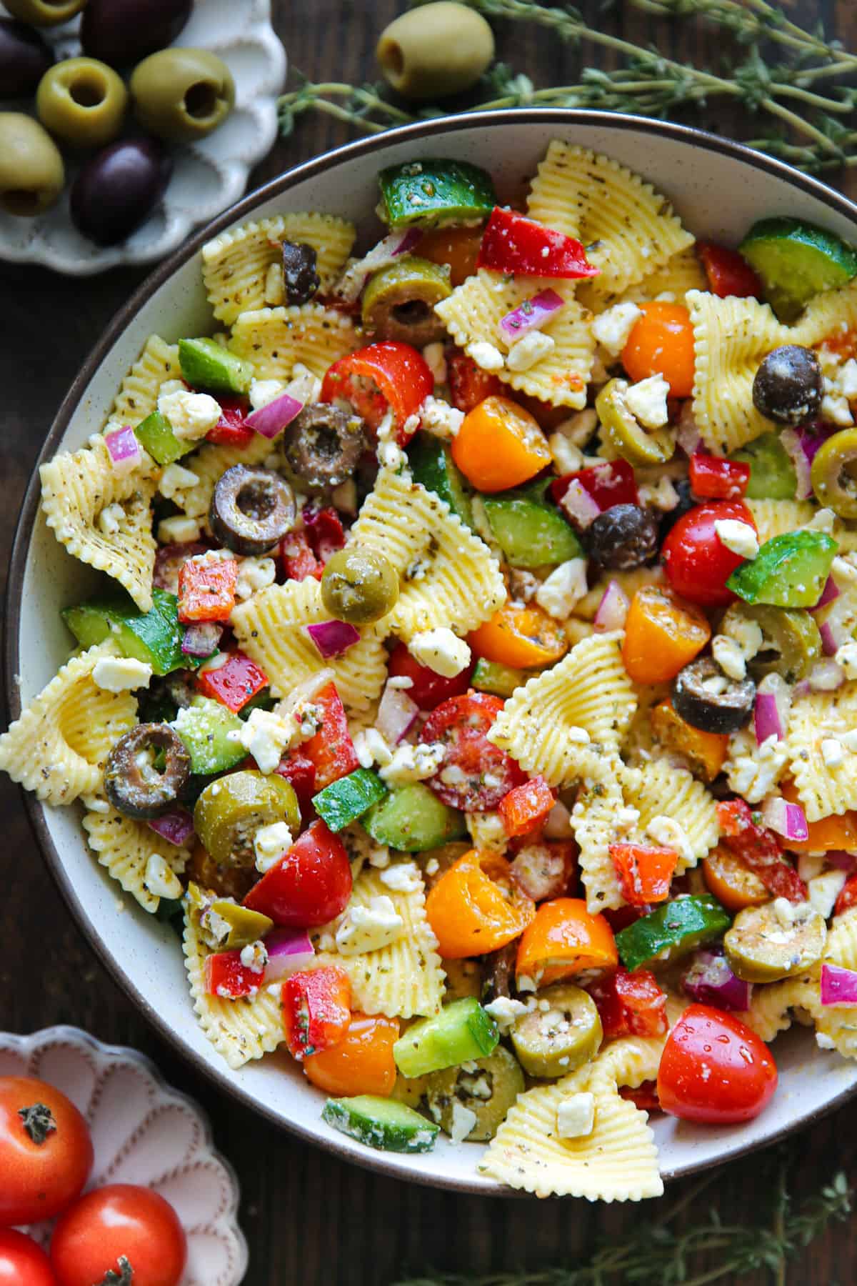 Greek pasta salad with tomatoes, cucumber, bell pepper, olives, red onions, and feta cheese - in a white bowl.