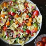 Greek pasta salad with tomatoes, cucumber, bell pepper, olives, red onions, and feta cheese - in a white bowl.