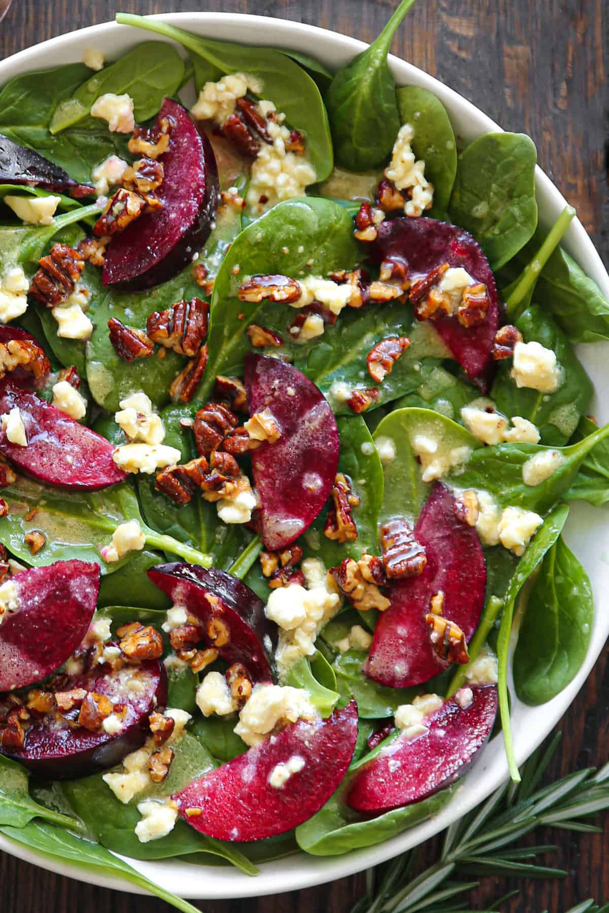 Plum Spinach Salad with Feta Cheese, Pecans, and Honey-Lemon Dressing - in a white bowl.