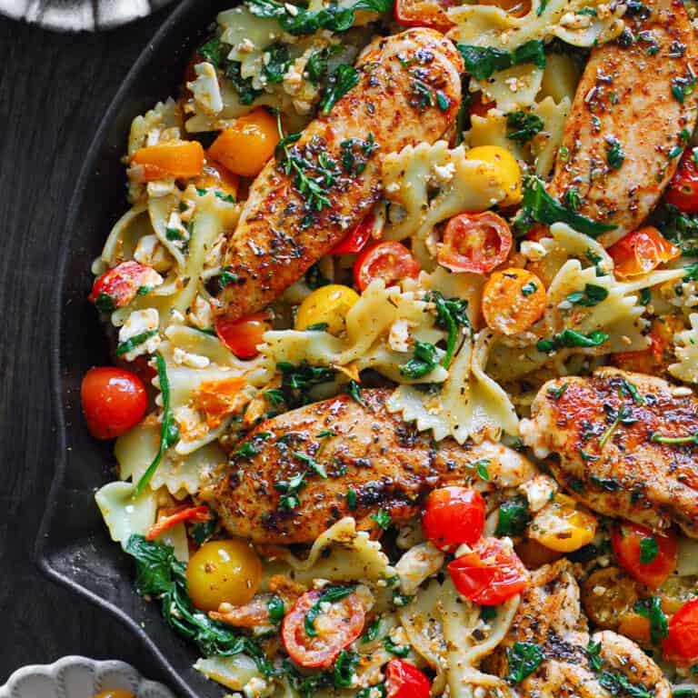 Chicken Feta Pasta with bow-tie pasta, tomatoes, and spinach - in a cast iron skillet.