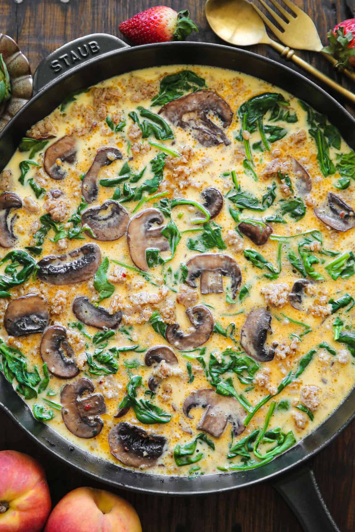 frittata ingredients (crumbled sausage, mushrooms, spinach, and eggs) in a cast iron skillet.