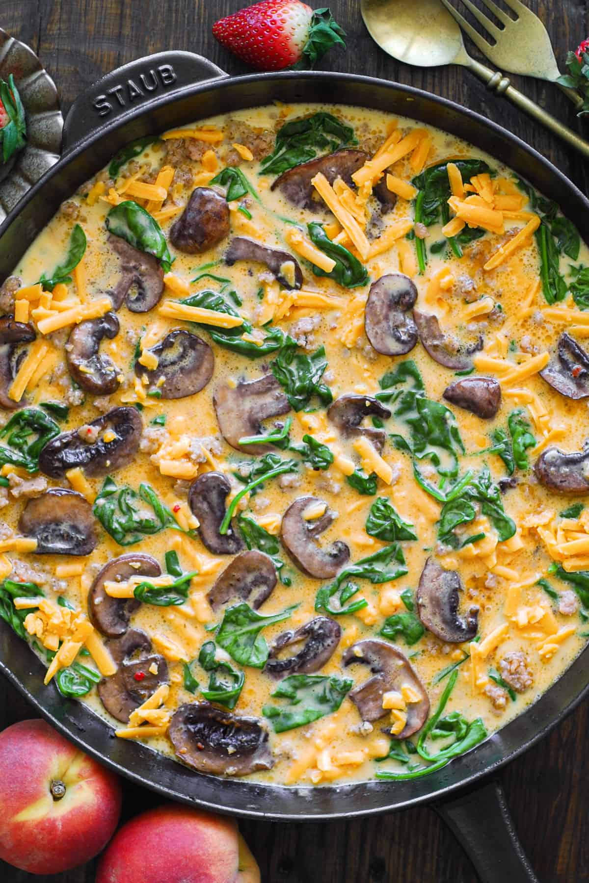 frittata ingredients (crumbled sausage, mushrooms, spinach, eggs, and shredded cheddar cheese) in a cast iron skillet.