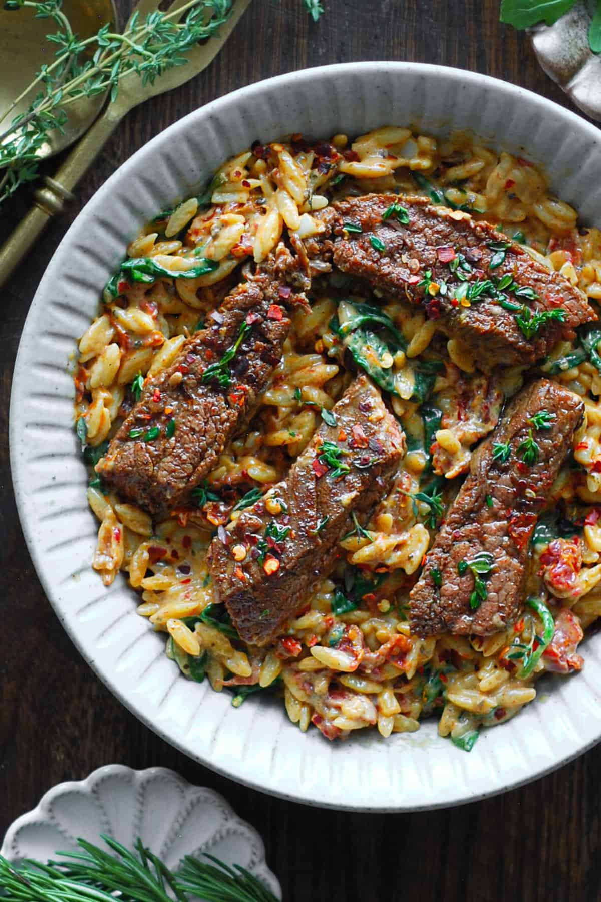 Pan-Seared Flank Steak (sliced) with Creamy Orzo, Spinach, and Sun-Dried Tomatoes - in a white bowl.
