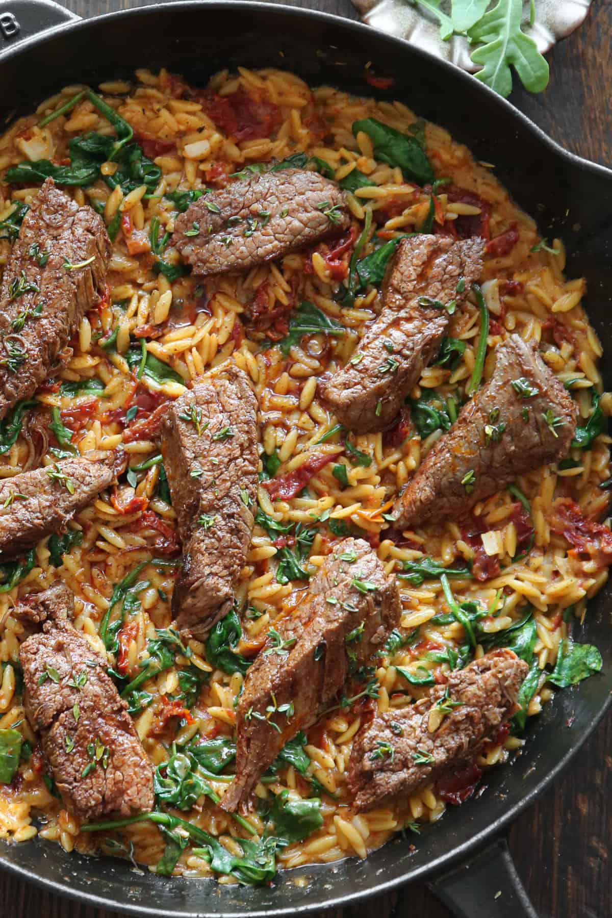 Pan-Seared Flank Steak (sliced) with Creamy Orzo, Spinach, and Sun-Dried Tomatoes - in a cast iron skillet.