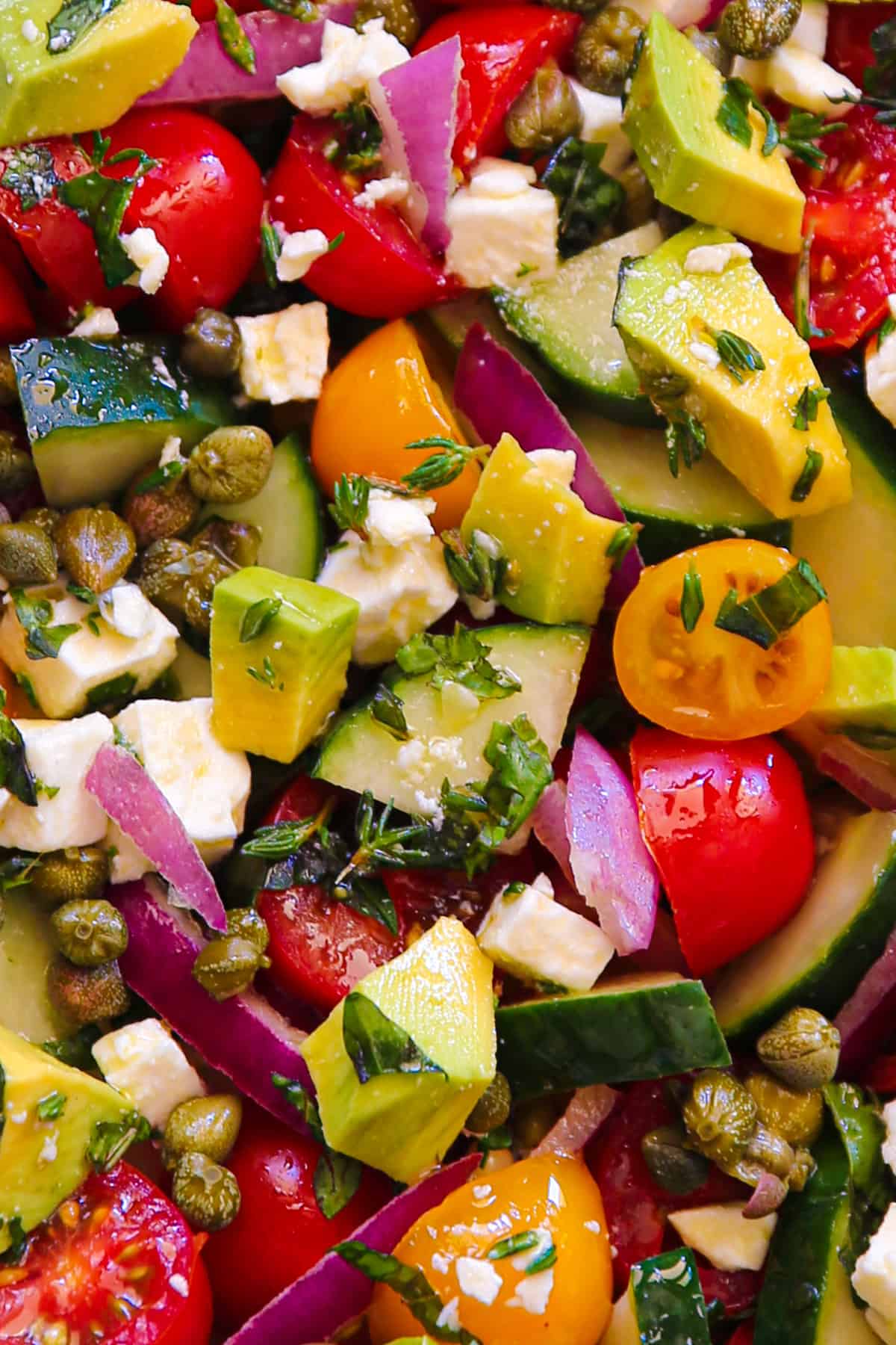 Greek Salad with tomatoes, cucumber, red onions, avocado, capers, and feta cheese - close-up photo.