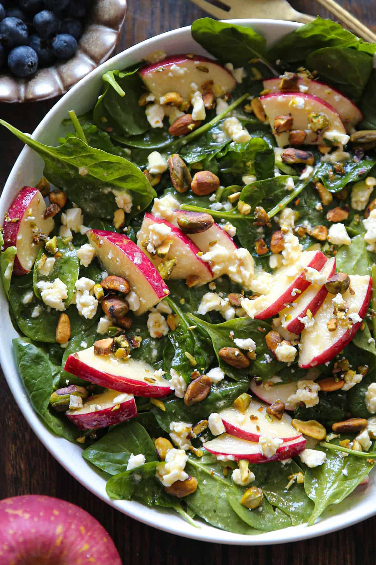 apple spinach salad with feta, pistachios, honey-mustard lemon dressing - in a white bowl.