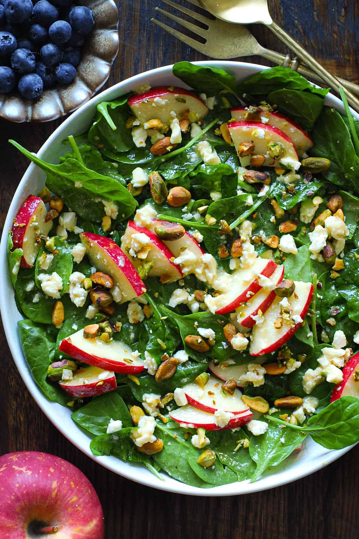 apple spinach salad with feta, pistachios, honey-mustard lemon dressing - in a white bowl.