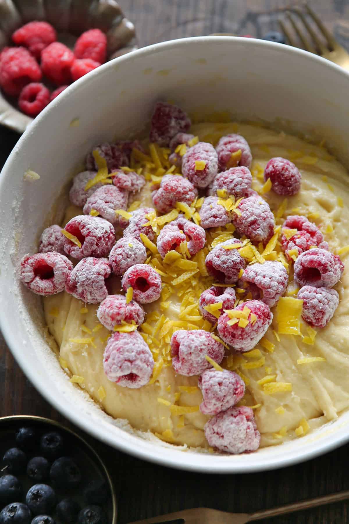 flour coated raspberries, lemon zest, and cake batter in a bowl.