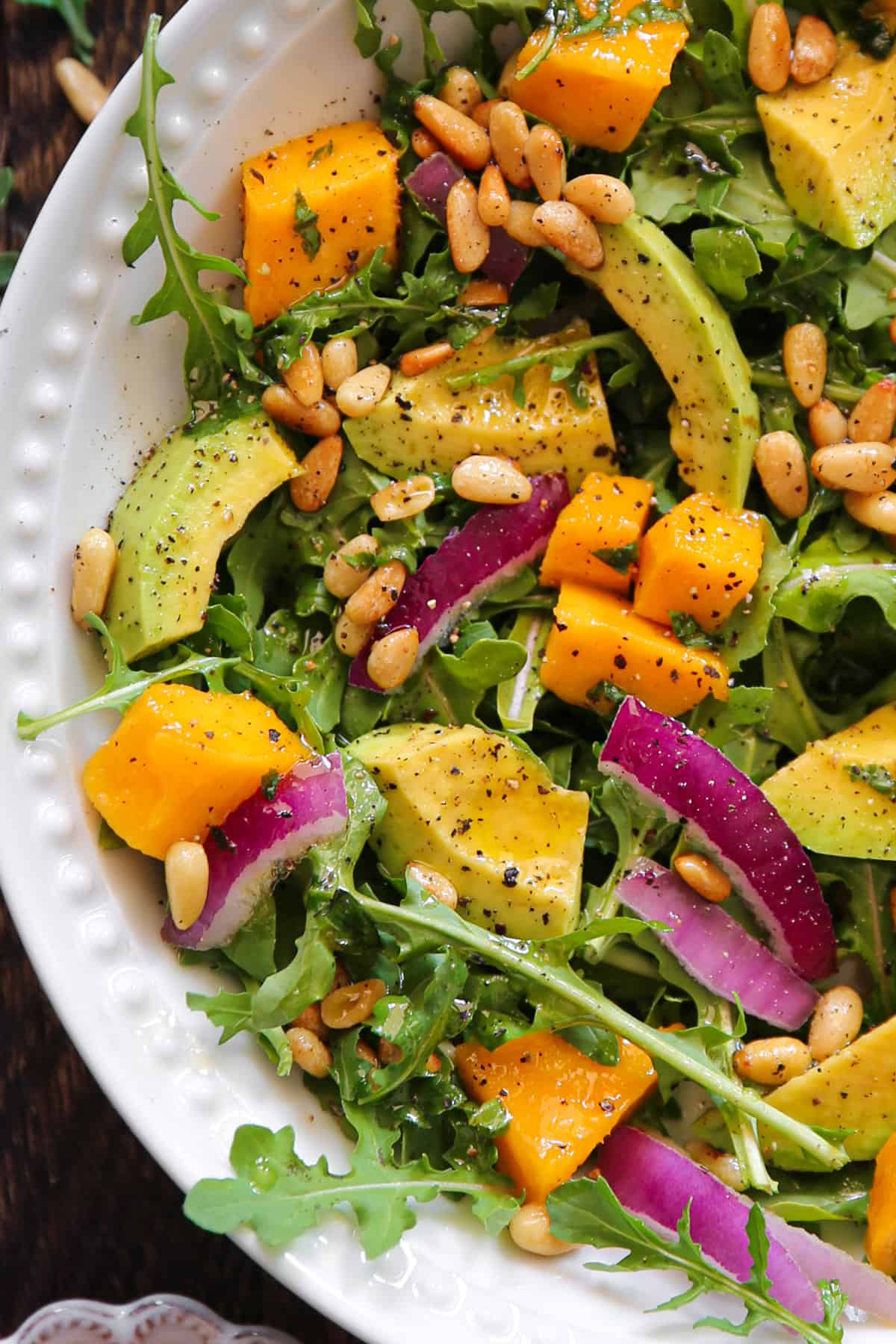 Avocado Mango Salad with Arugula, Pine Nuts and Honey Lime Dressing - in a white bowl.