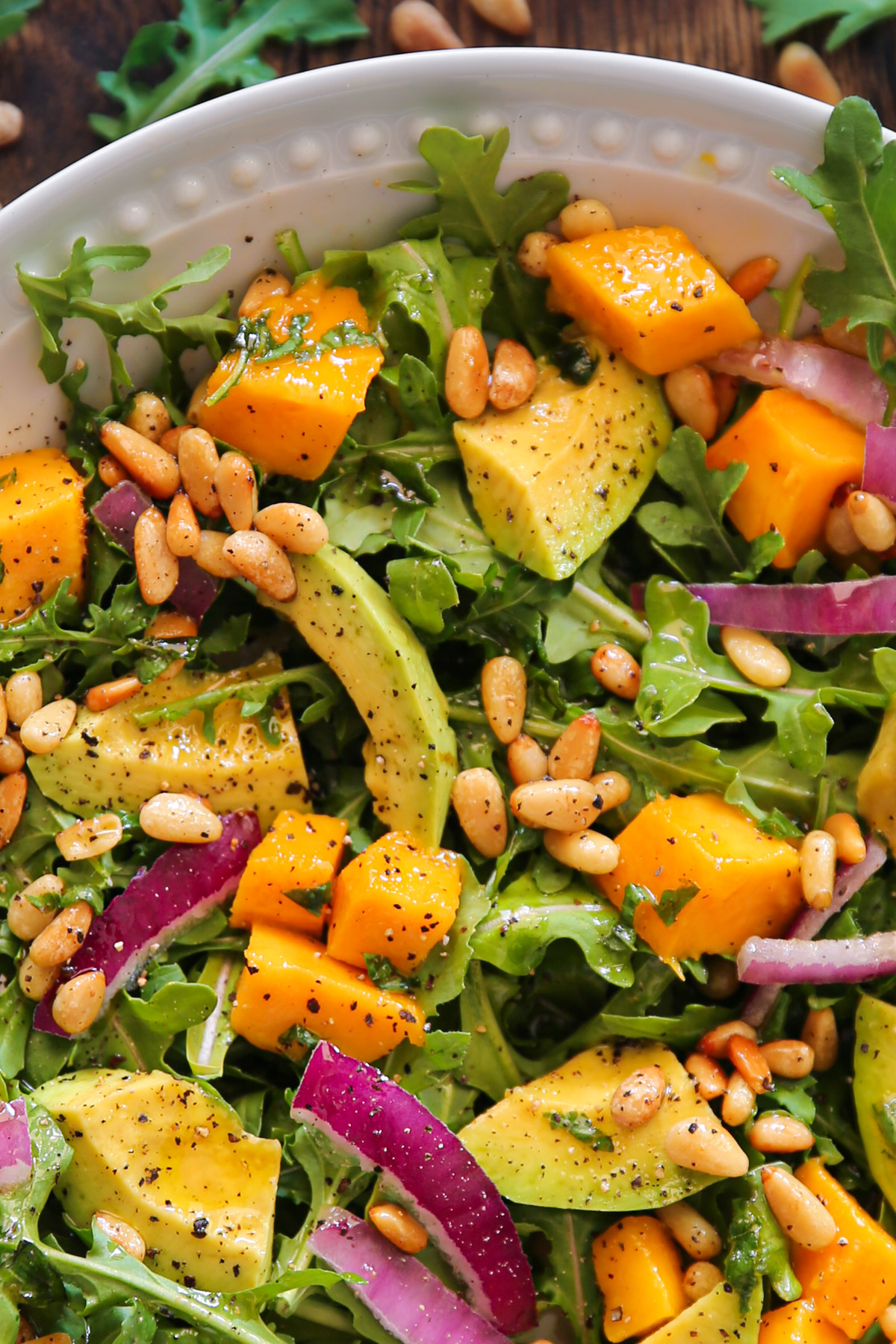 Avocado Mango Salad with Arugula, Pine Nuts, and Honey-Lime Dressing - in a white bowl (close-up photo).