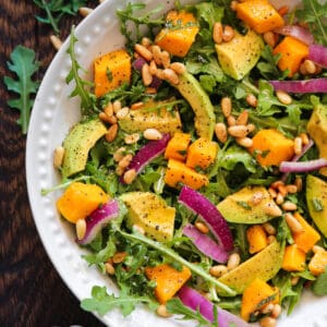 Avocado Mango Salad with Arugula, Pine Nuts, and Honey-Lime Dressing - in a white bowl.