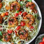 Garlic shrimp spaghetti with cherry tomatoes, olives, red onion, cucumber, feta cheese - in a white bowl.
