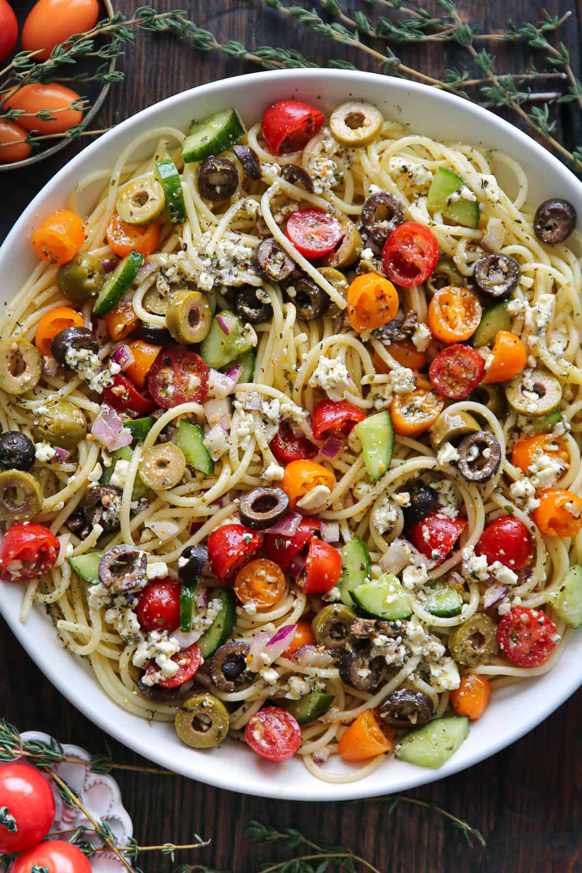 Spaghetti pasta with cherry tomatoes, olives, cucumber, red onions, and feta cheese - in a white bowl.