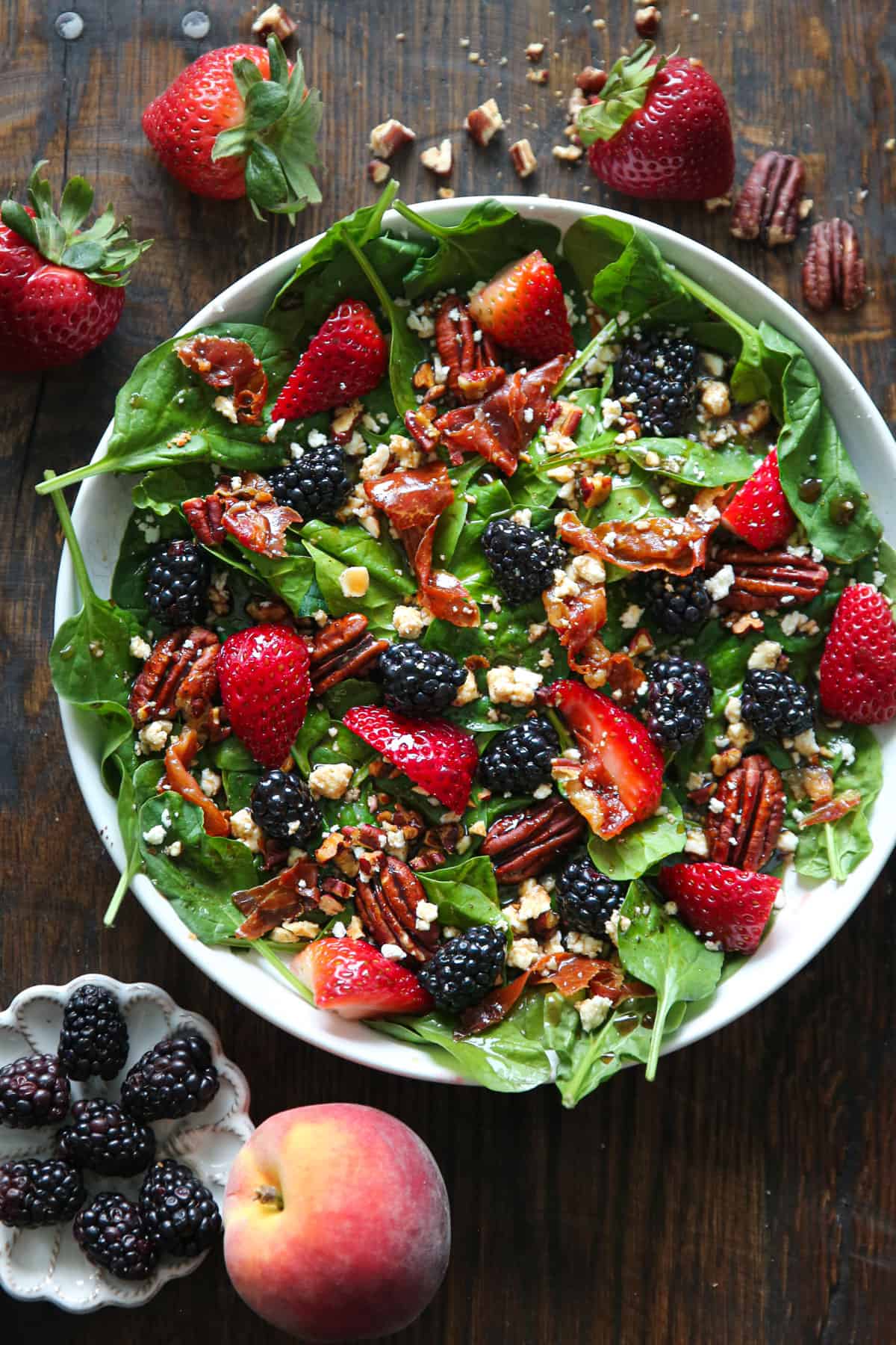 Berry spinach salad with strawberries, blackberries, feta cheese, pecans, crispy prosciutto, and balsamic glaze - in a white bowl.