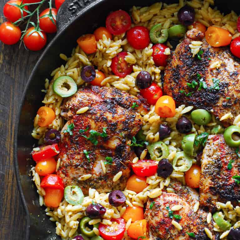 Greek Chicken Orzo with cherry tomatoes and olives - in a cast iron skillet.